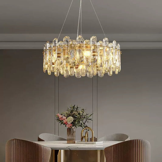Close-up view of a gold chandelier featuring clear crystals and internal LED lights, positioned above a dining table.