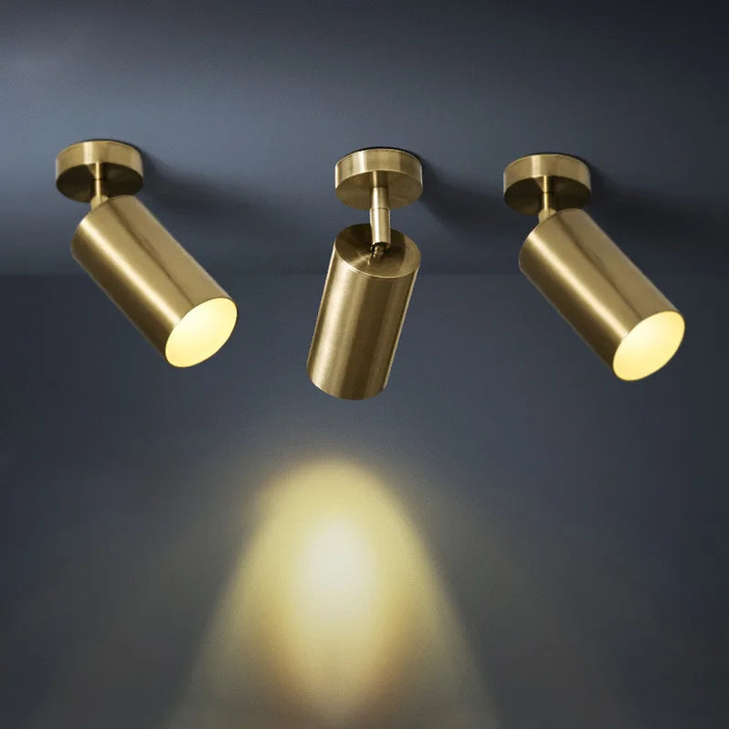 Close-up of brushed gold cylinder spotlights on a dark ceiling, casting light downwards.