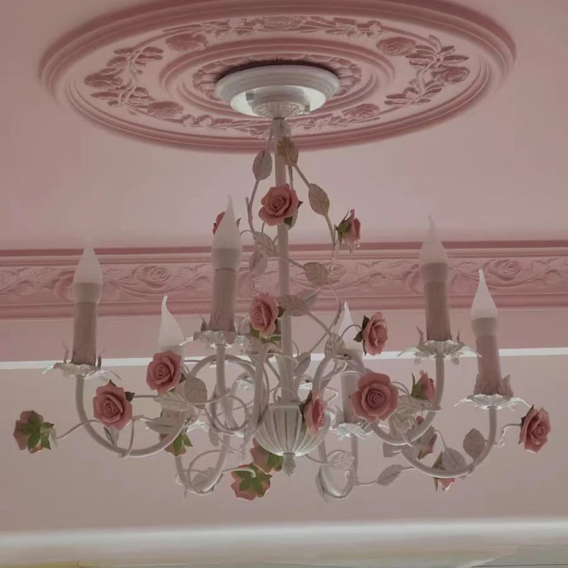 White iron chandelier with pink roses and green leaves, installed on a pink ceiling with decorative molding.