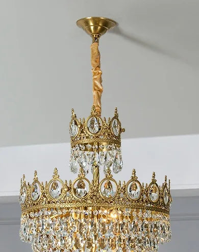 Gold chandelier hanging from a ceiling in a room with light-colored walls and a blue curtain.