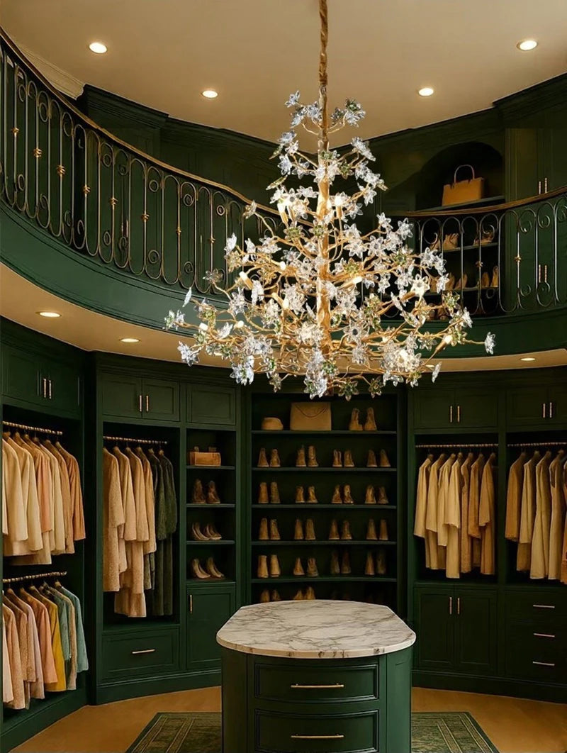 A grand, circular walk-in closet with dark green walls and built-in cabinetry, featuring a large, ornate gold chandelier with crystal floral accents hanging from the center.