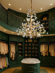 A grand, circular walk-in closet with dark green walls and built-in cabinetry, featuring a large, ornate gold chandelier with crystal floral accents hanging from the center.
