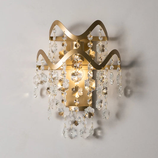 Close-up of a gold wall sconce featuring a wavy frame with hanging crystal prisms.