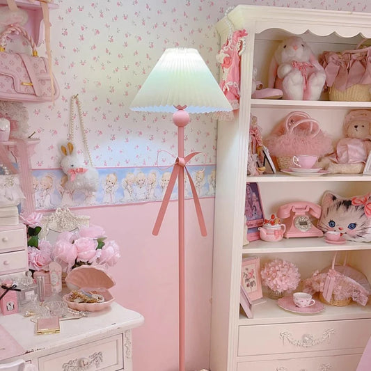 Close-up of a pink floor lamp with a pleated fabric shade and a pink bow, showcasing its decorative base.