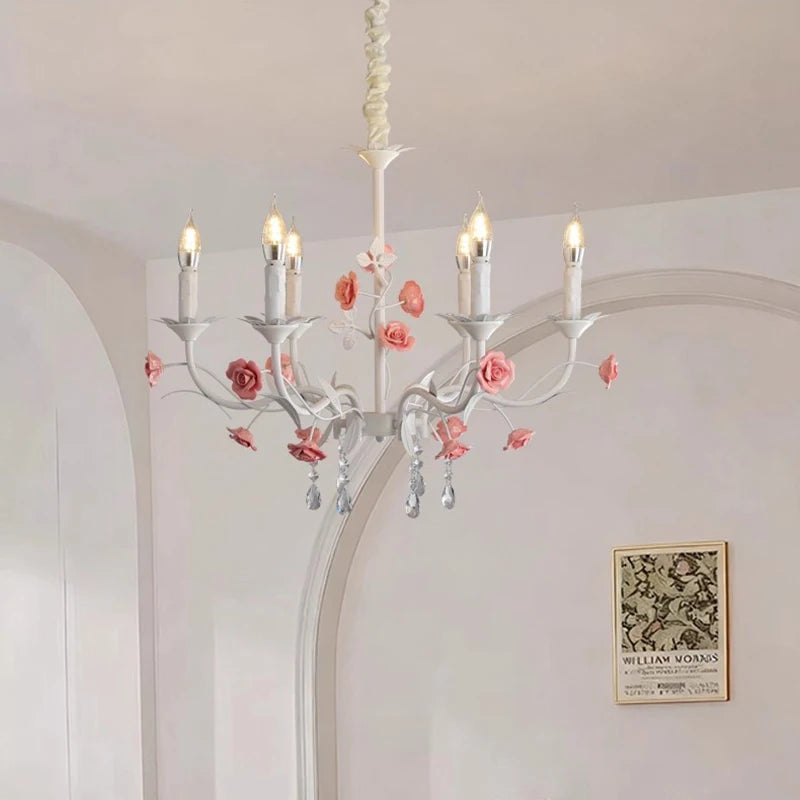 View of a white floral crystal candelabra chandelier with pink roses, mounted on a ceiling in a room with white paneled walls and artwork.