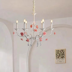 View of a white floral crystal candelabra chandelier with pink roses, mounted on a ceiling in a room with white paneled walls and artwork.