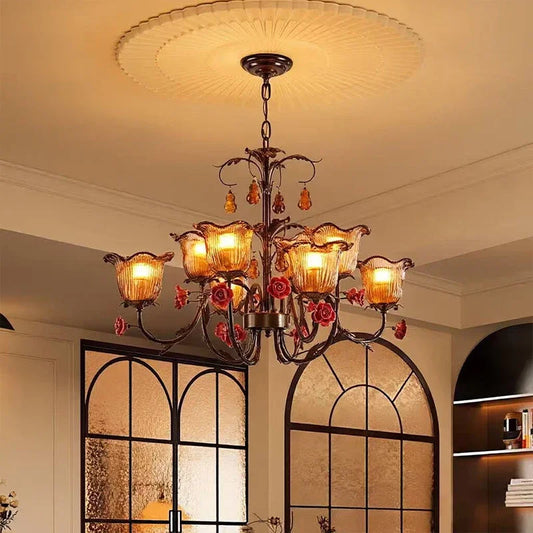 A bronze chandelier with red rose ceramic flowers and clear glass shades illuminates a room with arched windows.