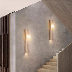 Two travertine stone wall sconces with frosted globes mounted on a textured wall next to a wooden staircase.