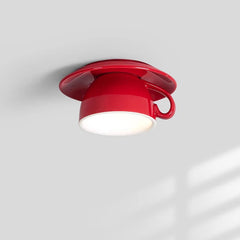 Red ceramic coffee cup shaped ceiling light fixture mounted on a white ceiling, emitting warm light from its interior.