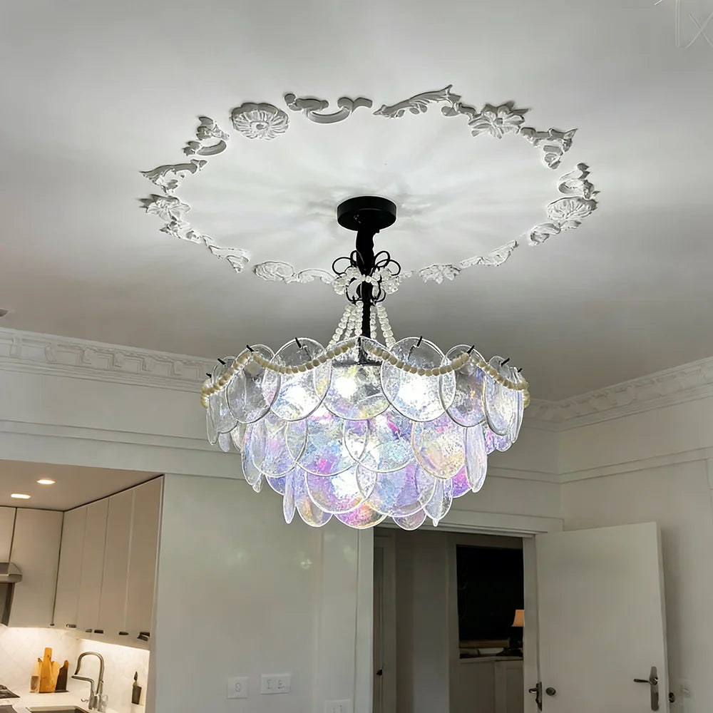 A multi-tiered glass chandelier with pearl accents suspended from a white ceiling with ornate molding.