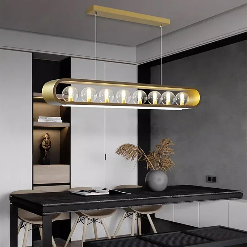 A contemporary gold pendant light with clear glass globes and an oval frame, installed over a dark wood dining table.