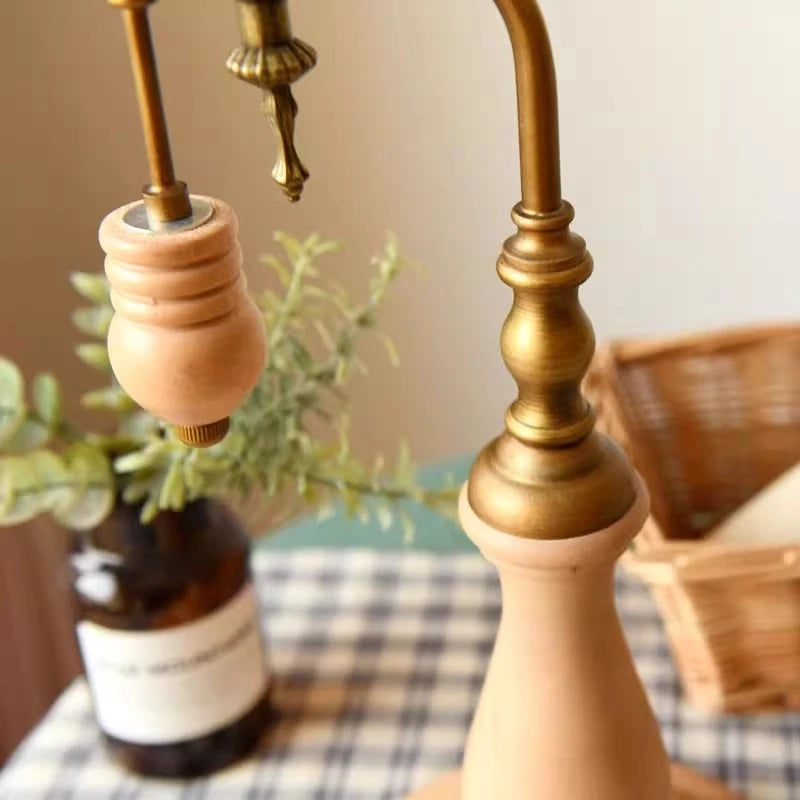 Decorative lamp with wooden and brass elements on a table with plants and a basket in the background.