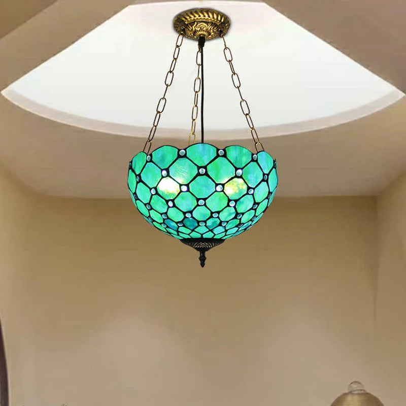 Close-up of a green Tiffany-style pendant light with a diamond pattern, illuminated from within, hanging from a decorative chain.