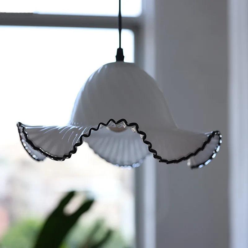 A white glass fluted pendant light with black trim hangs near a window with natural light, showcasing its shape.