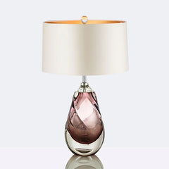 Purple glass swirl table lamp with a cream fabric shade reflecting on a surface