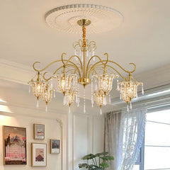 Gold crystal chandelier with floral-inspired arms and teardrop crystals, mounted on a white ceiling with decorative molding.