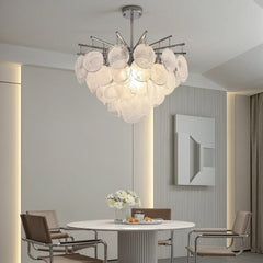 A modern chandelier with layered translucent white glass discs hanging from a chrome frame over a circular dining table.