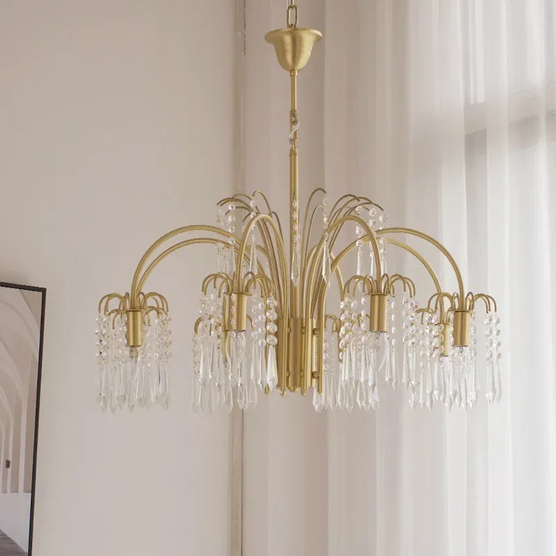 A wide shot of a gold crystal chandelier hanging in a well-lit room with sheer white curtains in the background.