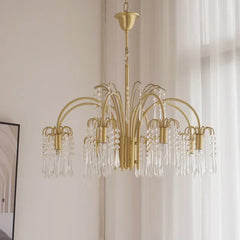 A wide shot of a gold crystal chandelier hanging in a well-lit room with sheer white curtains in the background.