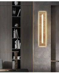 A modern wall sconce with a natural stone finish and a central LED light, mounted indoors next to a dark bookshelf.