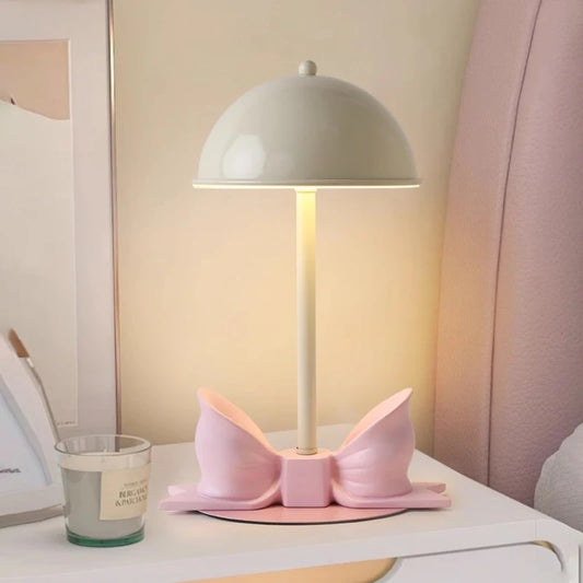 White dome shade table lamp with a pink bow accent sitting on a nightstand next to a candle.