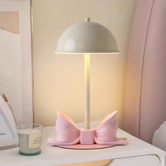 White dome shade table lamp with a pink bow accent sitting on a nightstand next to a candle.