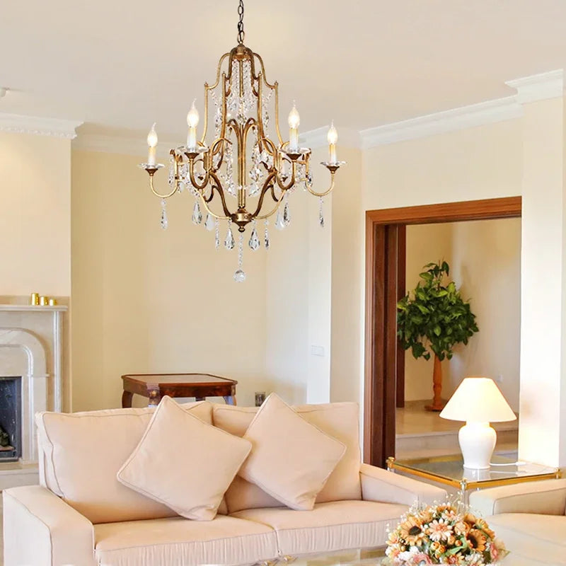 A gold candelabra crystal chandelier illuminating a living room with a sofa and fireplace.