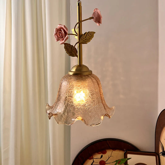 A pendant light with a fluted amber glass shade and a brass stem adorned with pink ceramic roses and green leaves.