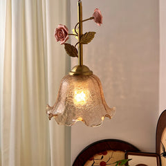 A pendant light with a fluted amber glass shade and a brass stem adorned with pink ceramic roses and green leaves.