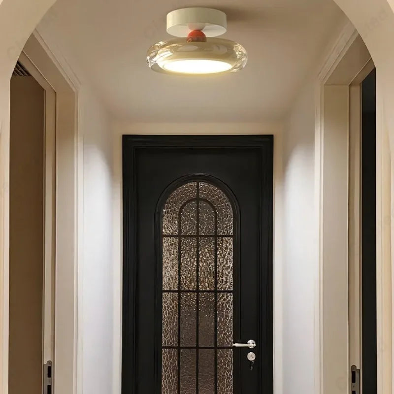 A contemporary flush mount ceiling light with a white base and a clear diffuser with a red accent, illuminating a hallway with a black arched door.