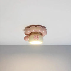 A pink ceramic coffee cup-shaped ceiling light with a pink bow and bubble-like trim, illuminated from below.