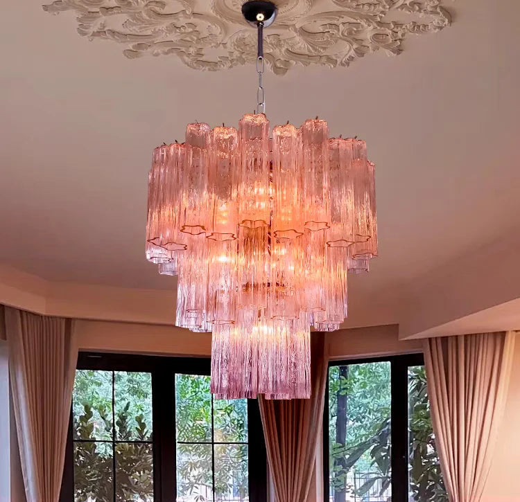 Pink chandelier hanging in a room with large windows and decorative ceiling.