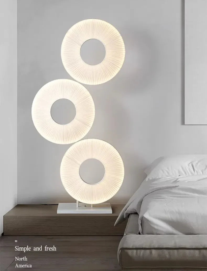 Modern lamp with three circular shades on a bedside table against a gray wall.