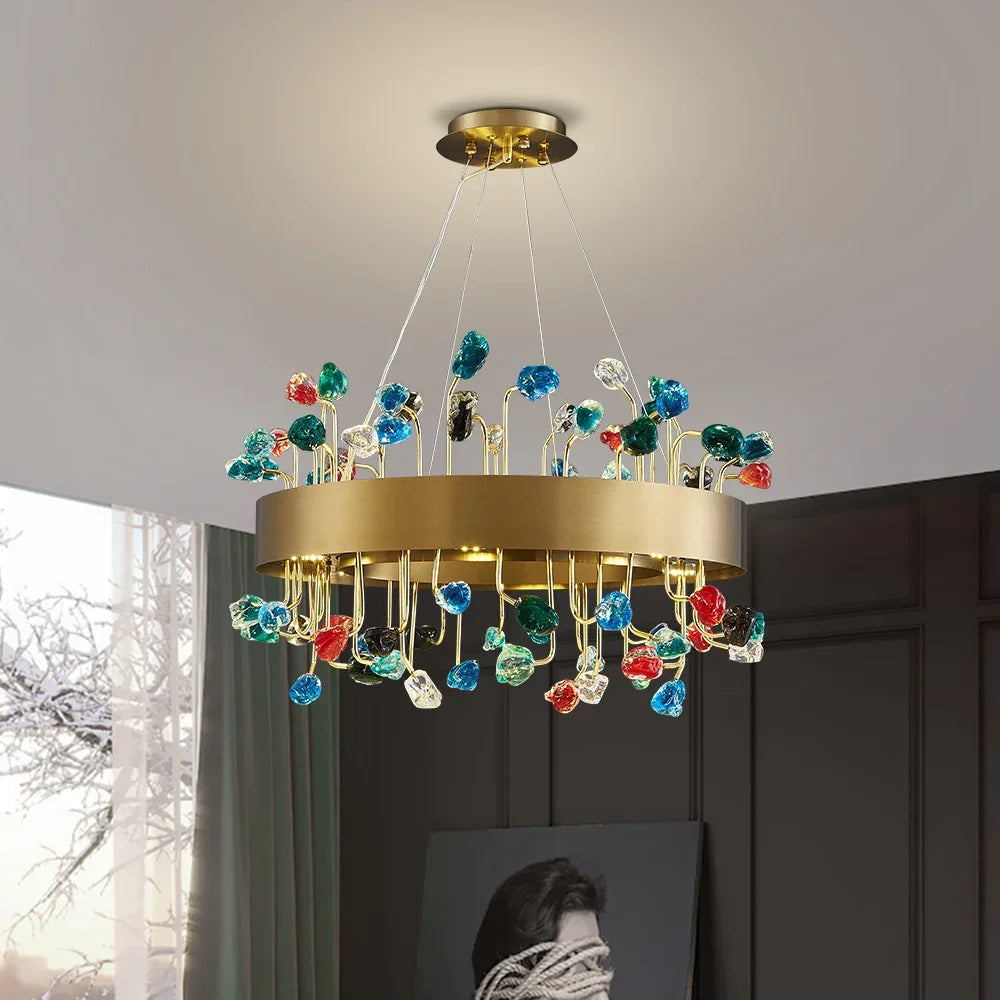 A round gold chandelier with colorful crystal accents hanging from the ceiling in a room.