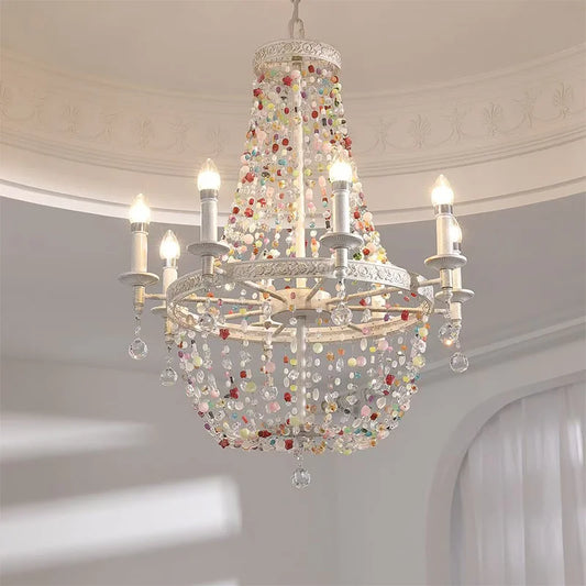 Close-up of a white multi-arm chandelier adorned with colorful beads and crystal drops, illuminated.