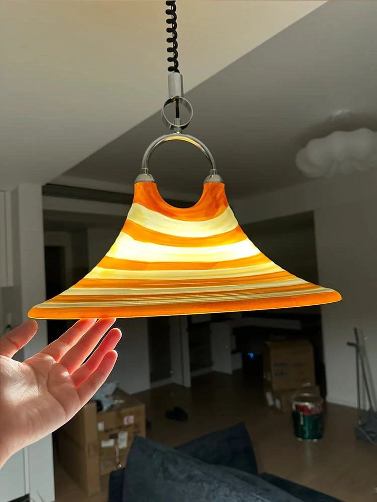 A hand holding the edge of the orange and white striped horn-shaped pendant light to show its scale and material.