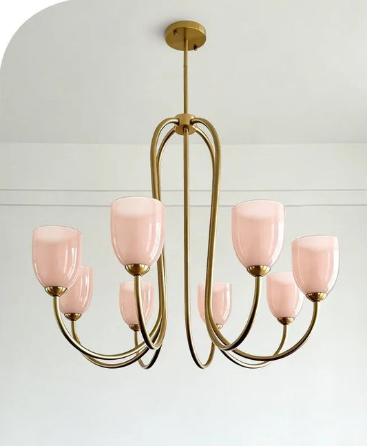Brushed gold chandelier with pink tulip glass shades hanging against a white background.