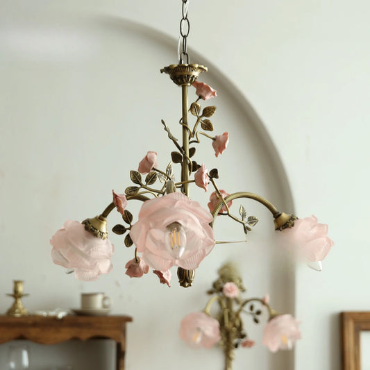 Close-up of a brass chandelier with pink rose bud accents and frosted glass shades.