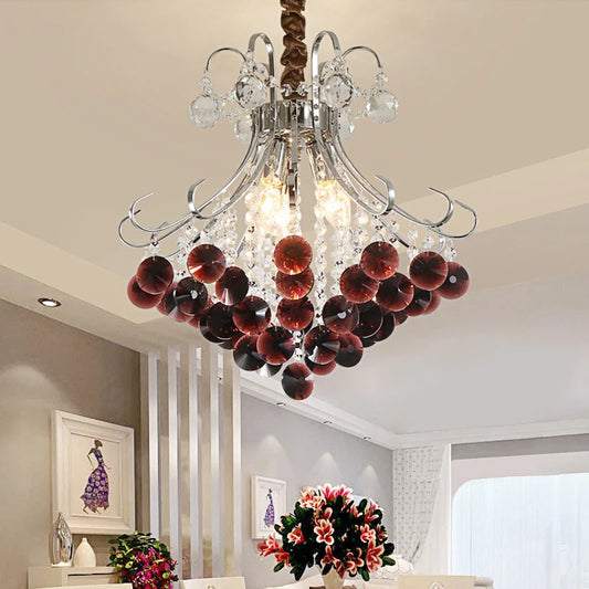 A crystal chandelier with wine red accents illuminating a dining room setting.