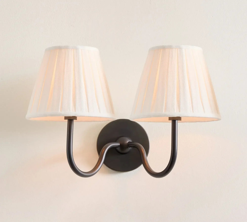 Wall-mounted lamp with two white lampshades on a light beige wall.