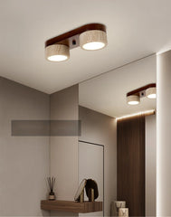 A hallway or bathroom with a modern flush mount ceiling light featuring two travertine stone cylinders on a dark wood base, reflected in a large mirror.