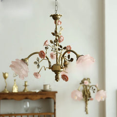 A brass chandelier adorned with pink rose buds and ceramic flowers, hanging against a white wall.