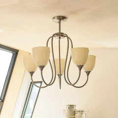 A gold-toned chandelier with three pink glass shades, shown in a room setting near a window.