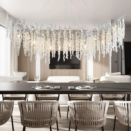 Curved chandelier with numerous clear crystal teardrops hanging from dark branches, suspended over a dining table.