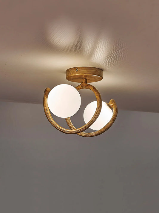 Close-up of a brushed gold semi-flush ceiling light with two intertwined swirls, each holding a frosted white globe.