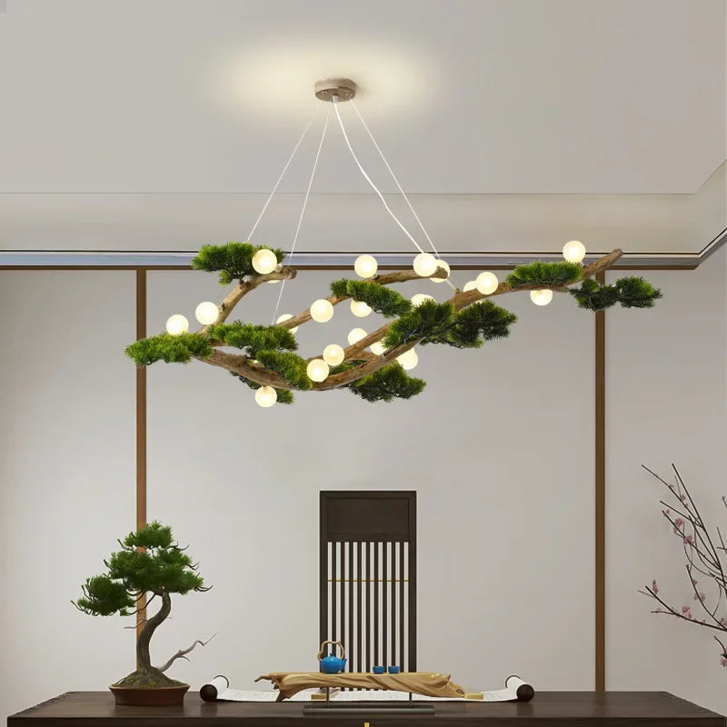 Close-up of a branch-shaped chandelier featuring numerous small LED lights and artificial greenery, showcasing the wood texture and the suspension wires against a white ceiling.
