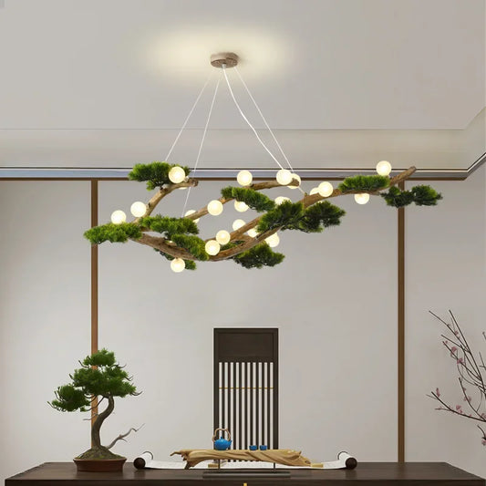 Close-up of a branch-shaped chandelier featuring numerous small LED lights and artificial greenery, showcasing the wood texture and the suspension wires against a white ceiling.