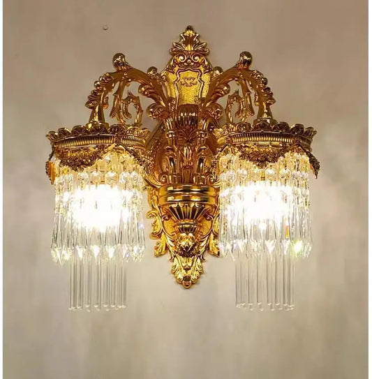 A golden wall sconce with two illuminated tiers of crystal pendants, showcasing the warm light emanating from within.