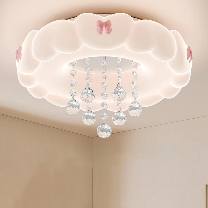 A white cloud-shaped flush mount ceiling light with pink bows and hanging crystal spheres, casting a gentle glow.