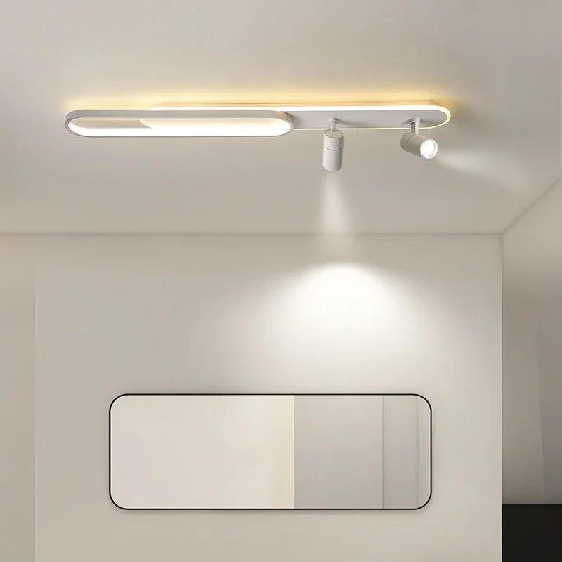 White linear ceiling lamp with an oval accent and two spotlight fixtures casting light downwards onto a rectangular mirror below.